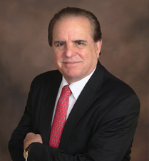 Frank Giotto, President and CEO of Fiber Instrument Sales smiling with his arms crossed in front.  Wearing a black suit jacket, white shirt and red tie